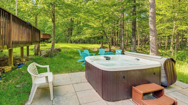 Ein Whirlpool in einem von Bäumen umgebenen Garten mit einer Holzterrasse, Stühlen und einer kleinen Holzhütte.