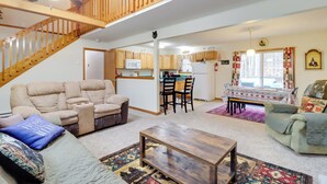 Ein geräumiger Wohnbereich mit einer Couch, einem Couchtisch und einem Esstisch mit Stühlen. Eine Holztreppe verbindet den Wohnbereich mit einer oberen Ebene.