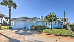 A light blue single-story house with a garage, a small front yard with a palm tree, and a clear blue sky. - Modern Seaview House - 200 Yards to Daytona Beach! (Daytona Beach)