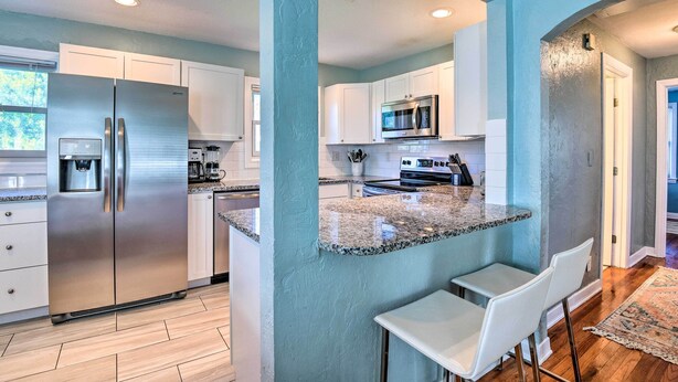 A modern kitchen with stainless steel appliances, a granite countertop, and white bar stools. - Modern Seaview House - 200 Yards to Daytona Beach! (Daytona Beach)