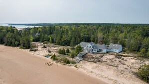 Una casa grande con un muelle, rodeada de un bosque frondoso y una playa arenosa.