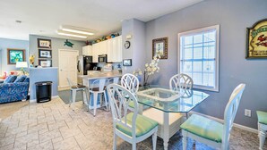 A dining area with a glass table and white chairs, a kitchen with white cabinets, and a living room with a blue sofa. - Spacious North Topsail Family Home With 2 Decks (Sneads Ferry)