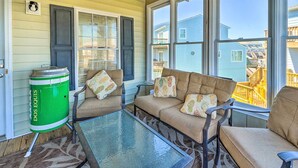 A cozy outdoor seating area with a glass table, cushioned chairs, and a green trash can labeled "DOS EQUIS". - Spacious North Topsail Family Home With 2 Decks (Sneads Ferry)