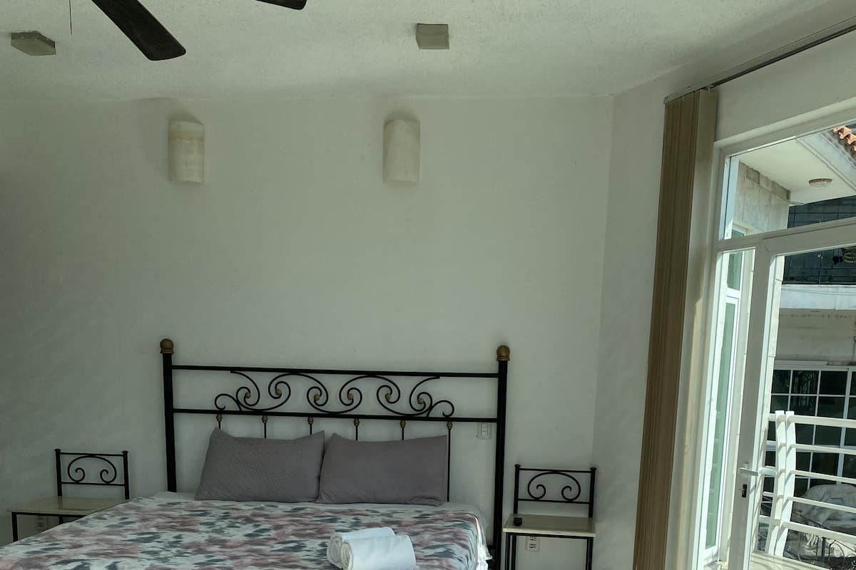 A bedroom with a bed, two bedside tables, a ceiling fan, and a large window.
