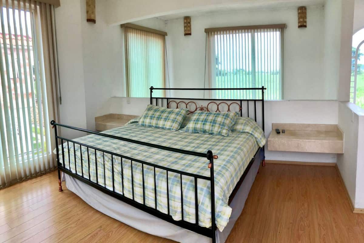 A bedroom with a metal bed frame, checkered bedding, a wooden floor, and a window with blinds.