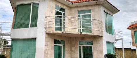 A two-story house with a balcony, large windows, and a tiled roof.