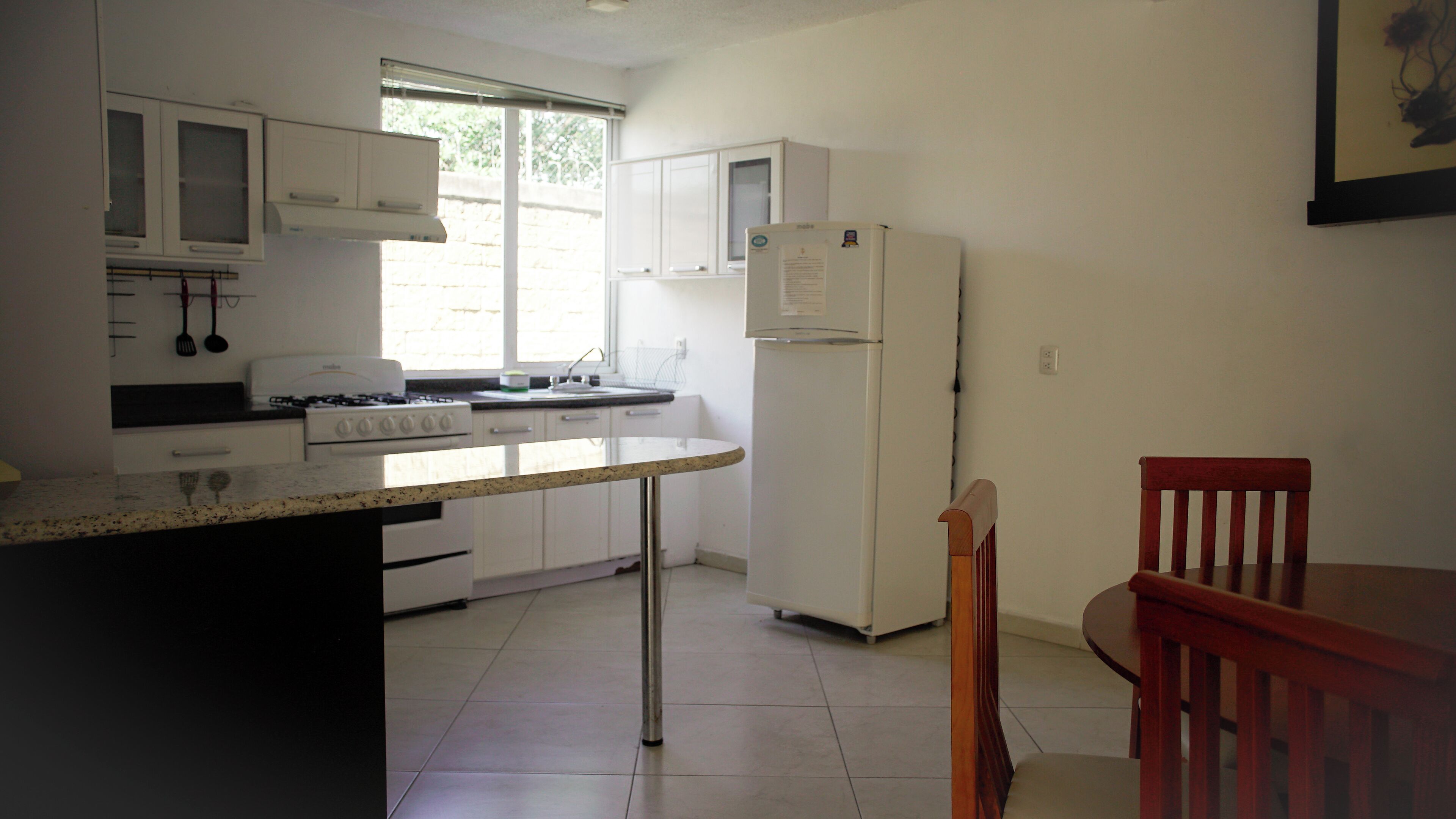 A kitchen with white cabinets, a stove, a refrigerator, and a dining table with a chair.