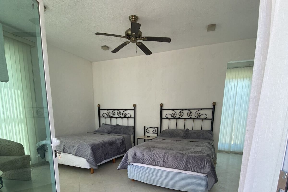 A room with two beds, a ceiling fan, and a sliding glass door leading to a balcony.