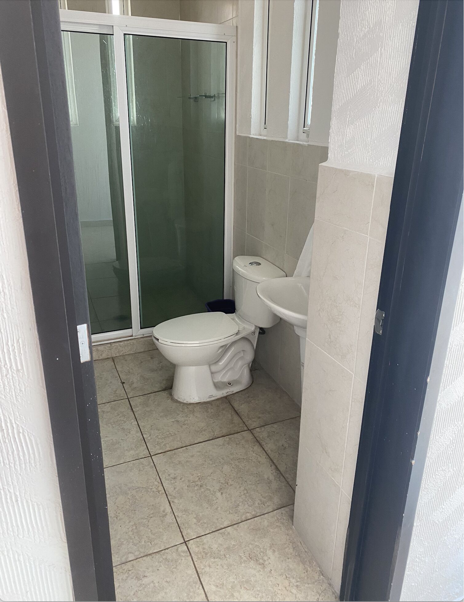 Un baño con inodoro, lavamanos y ducha con mampara de vidrio.