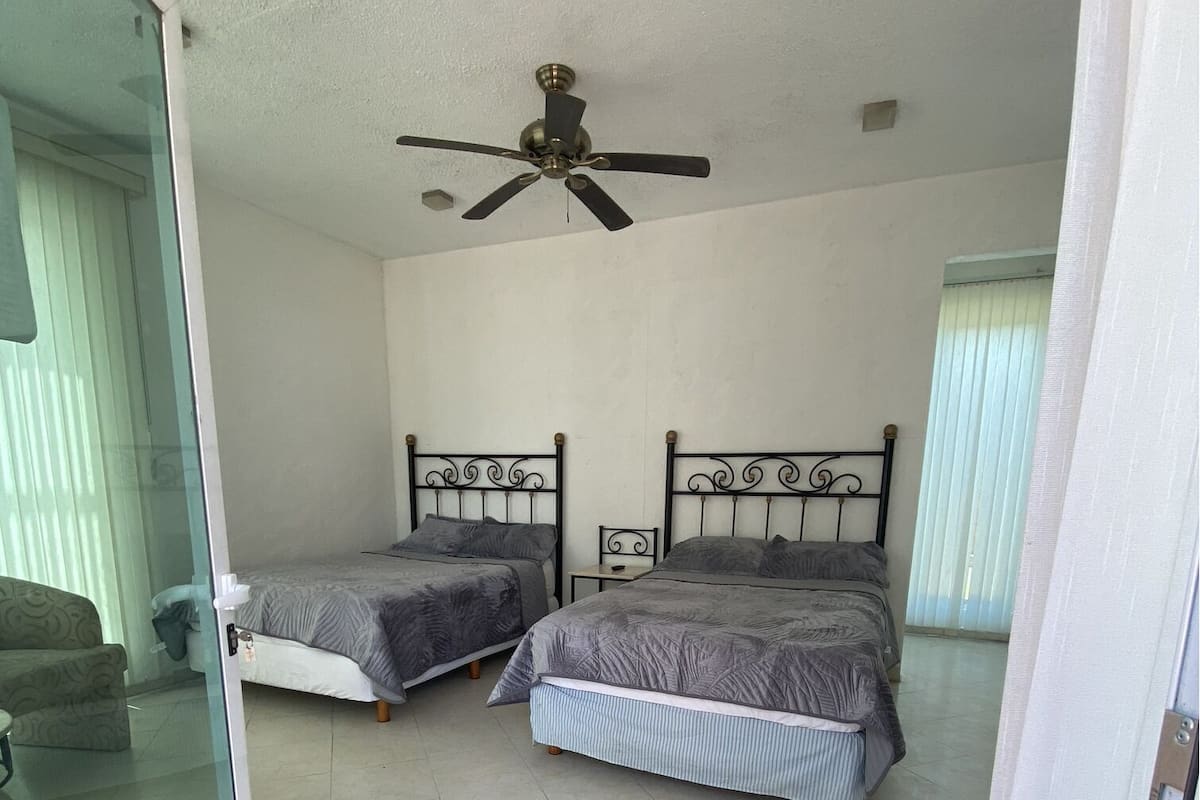 A bedroom with two beds, a ceiling fan, and a sliding glass door leading to a balcony.