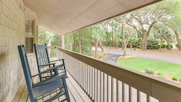 A covered porch with wooden railings, a bench, and a view of a road and trees.