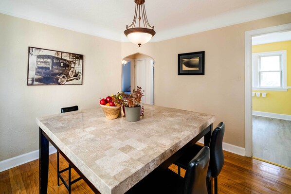 A dining area with a marble table, chairs, a chandelier, a fruit bowl, and a potted plant.