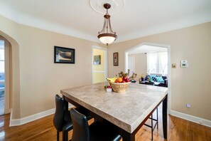 A dining area with a marble table, black chairs, a fruit bowl, and a hanging light fixture. - Ferndale Apartment w/ Yard - Near the Detroit Zoo! (Ferndale)