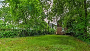 A grassy backyard with a brick house and a fence. - Ferndale Apartment w/ Yard - Near the Detroit Zoo! (Ferndale)