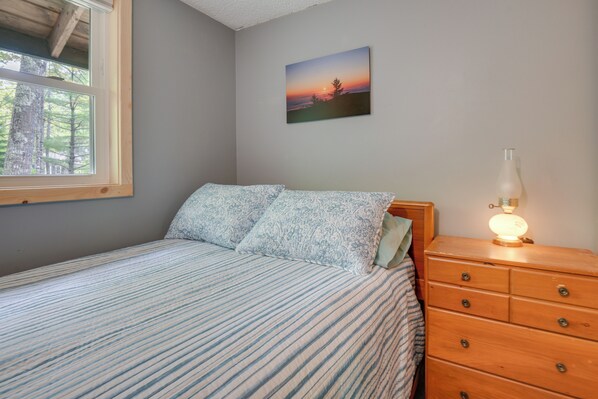 A bedroom with a bed, a dresser, a lamp, and a painting on the wall.