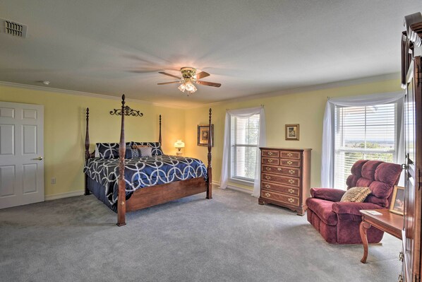 A bedroom with a four-poster bed, a wooden dresser, a red armchair, and a ceiling fan. - Patio & Covered Porch: Spacious Bellevue Home! (Bellevue)