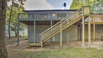 A wooden deck with a staircase leading to a covered area, surrounded by trees and a grassy area.