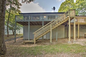 A wooden deck with a staircase leading to a covered area, surrounded by trees and a grassy area. - Furnished Deck & Grill: Hot Springs House (Hot Springs Village)