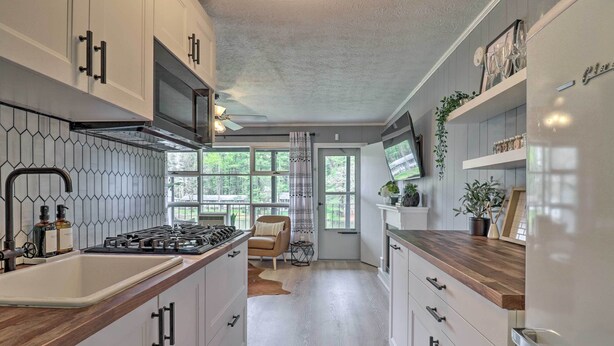 Une cuisine moderne avec des armoires blanches, un comptoir en bois et une cuisinière intégrée. Une fenêtre offre une vue sur la verdure environnante.