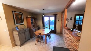 Un comedor con mesa y sillas de madera, una cocina con pared de ladrillo, y vistas a través de un ventanal.