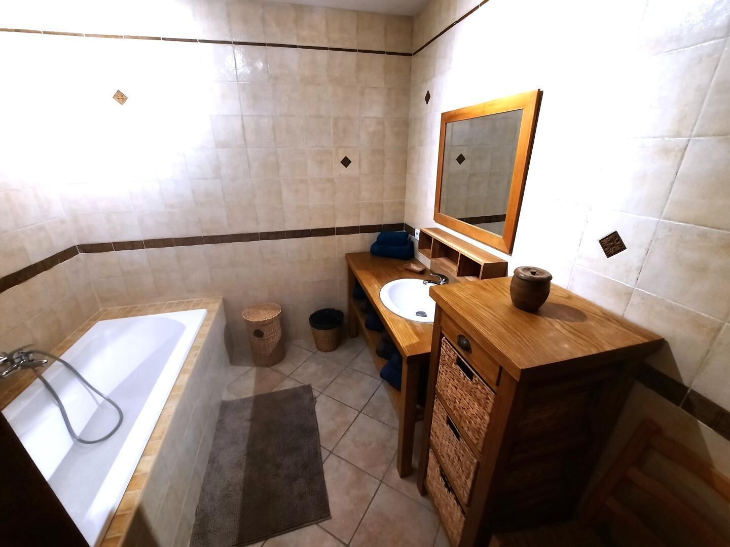 A bathroom with a bathtub, sink, mirror, and wooden vanity.