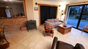Una sala de estar acogedora con una chimenea de ladrillo, un sofá, una mesa de centro de madera y un amplio ventanal corredera que da a un espacio exterior.