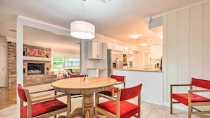 A spacious dining area with a wooden table and red upholstered chairs, a brick fireplace, and a modern kitchen in the background.