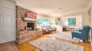 A living room with a brick fireplace, wooden flooring, and two large area rugs.