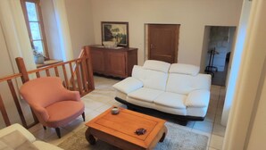 Ein Wohnzimmer mit einem weißen Sofa, einem rosa Sessel, einem Holztisch und einem Schrank mit einem Gemälde.