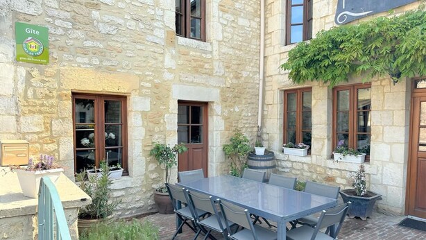 Ein Steinhaus mit Innenhof, einem Tisch mit Stühlen und Kübelpflanzen.