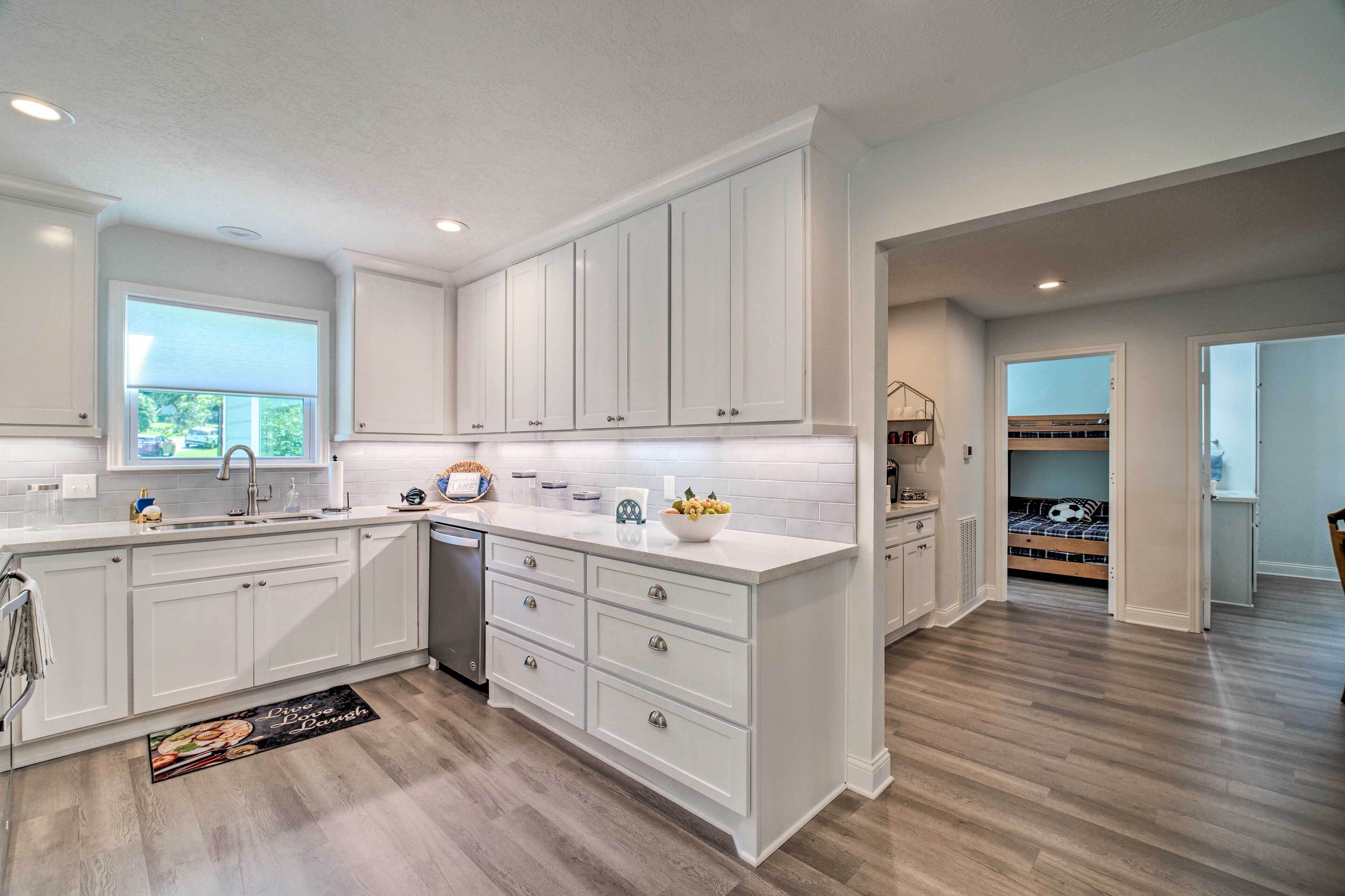 A modern kitchen with white cabinetry, a central island, and a view into a bedroom.