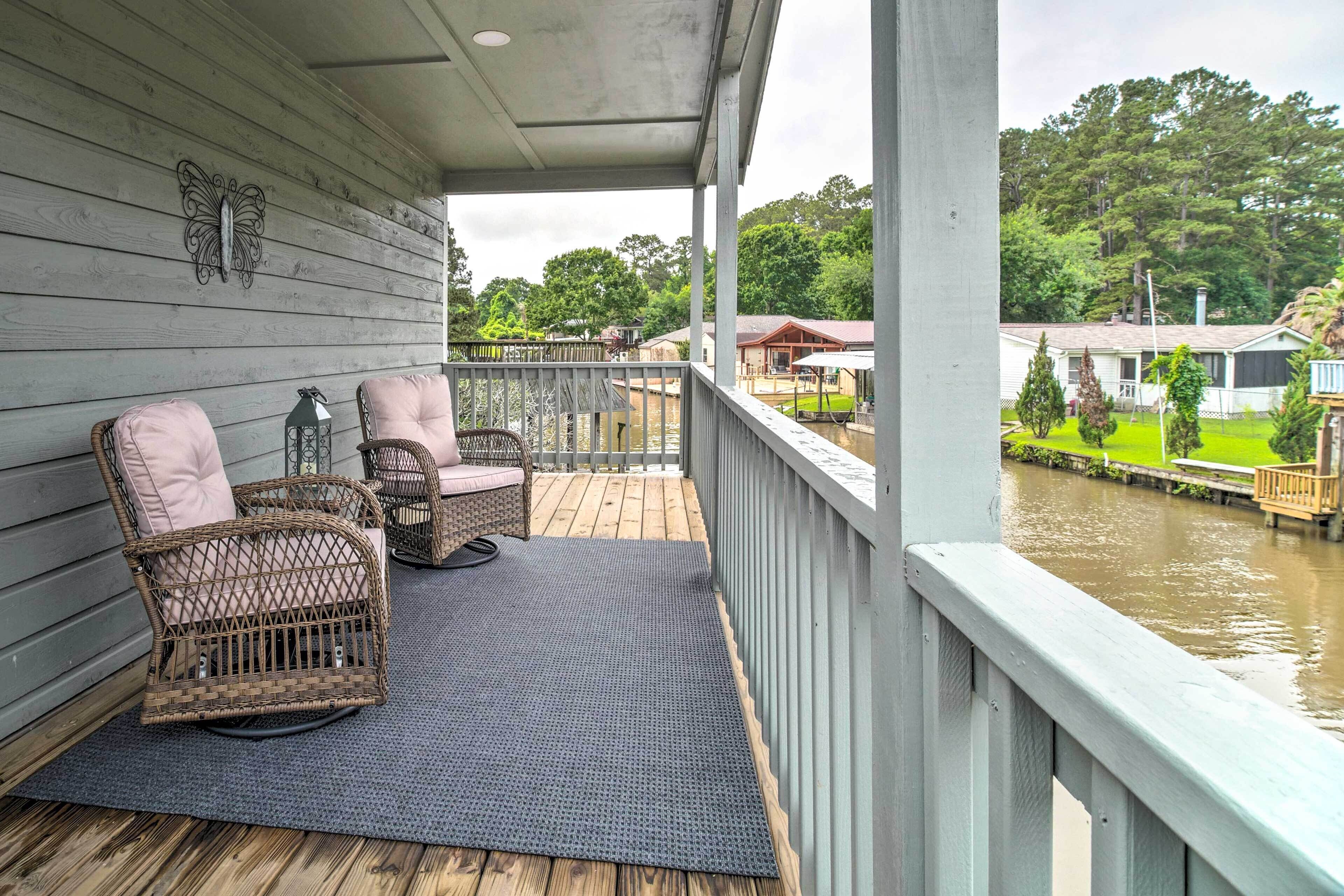 A wooden deck with wicker chairs and a view of a river and houses in the background.