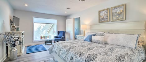 A bedroom with a large bed, a ceiling fan, a window, and a door leading to another room.