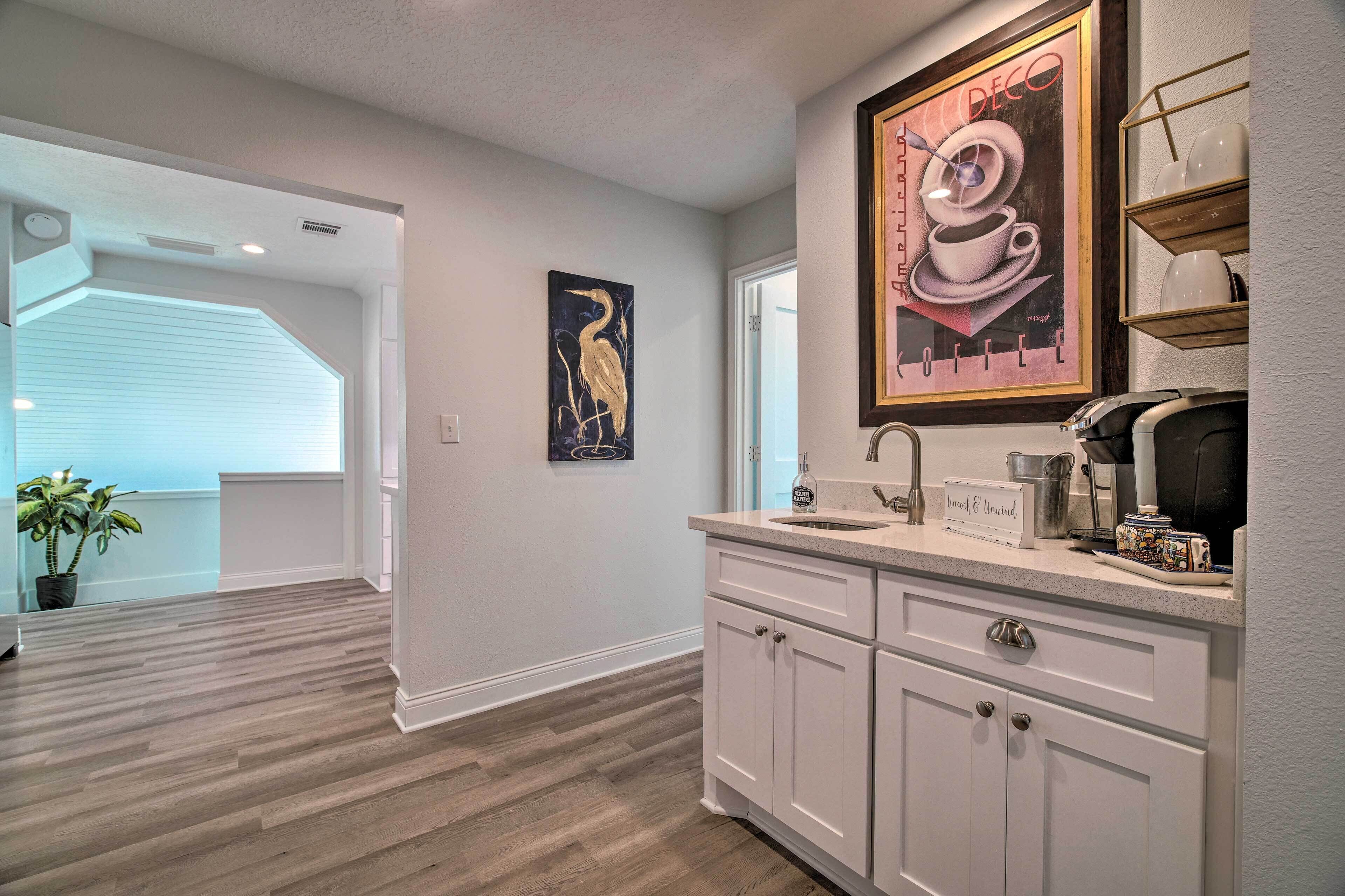 A modern kitchen with white cabinetry, a countertop with a coffee maker, and a framed artwork above the sink.