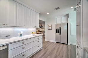 A modern kitchen with white cabinetry, a stainless steel refrigerator, and a countertop with a fruit bowl. - Bright Home w/ Dock on Lake Conroe! (Willis)