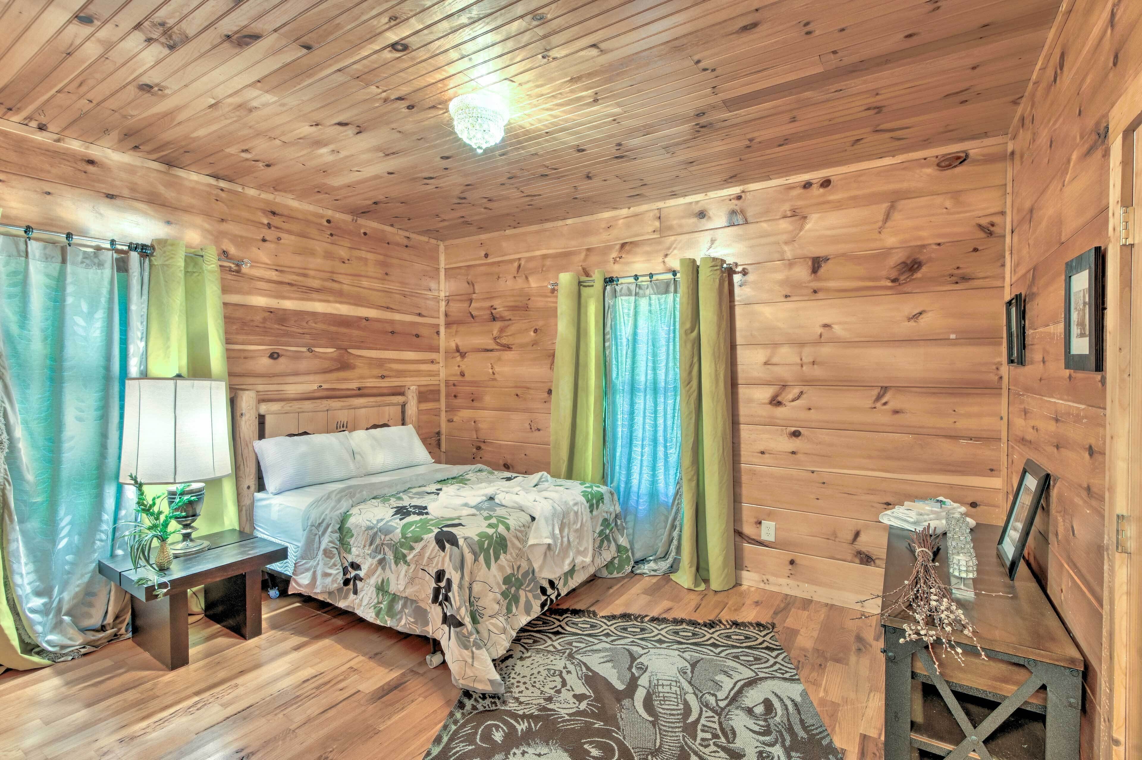 A wooden cabin room with a bed, a nightstand, a lamp, and curtains.