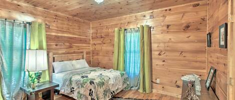 A wooden cabin room with a bed, a nightstand, a lamp, and curtains.