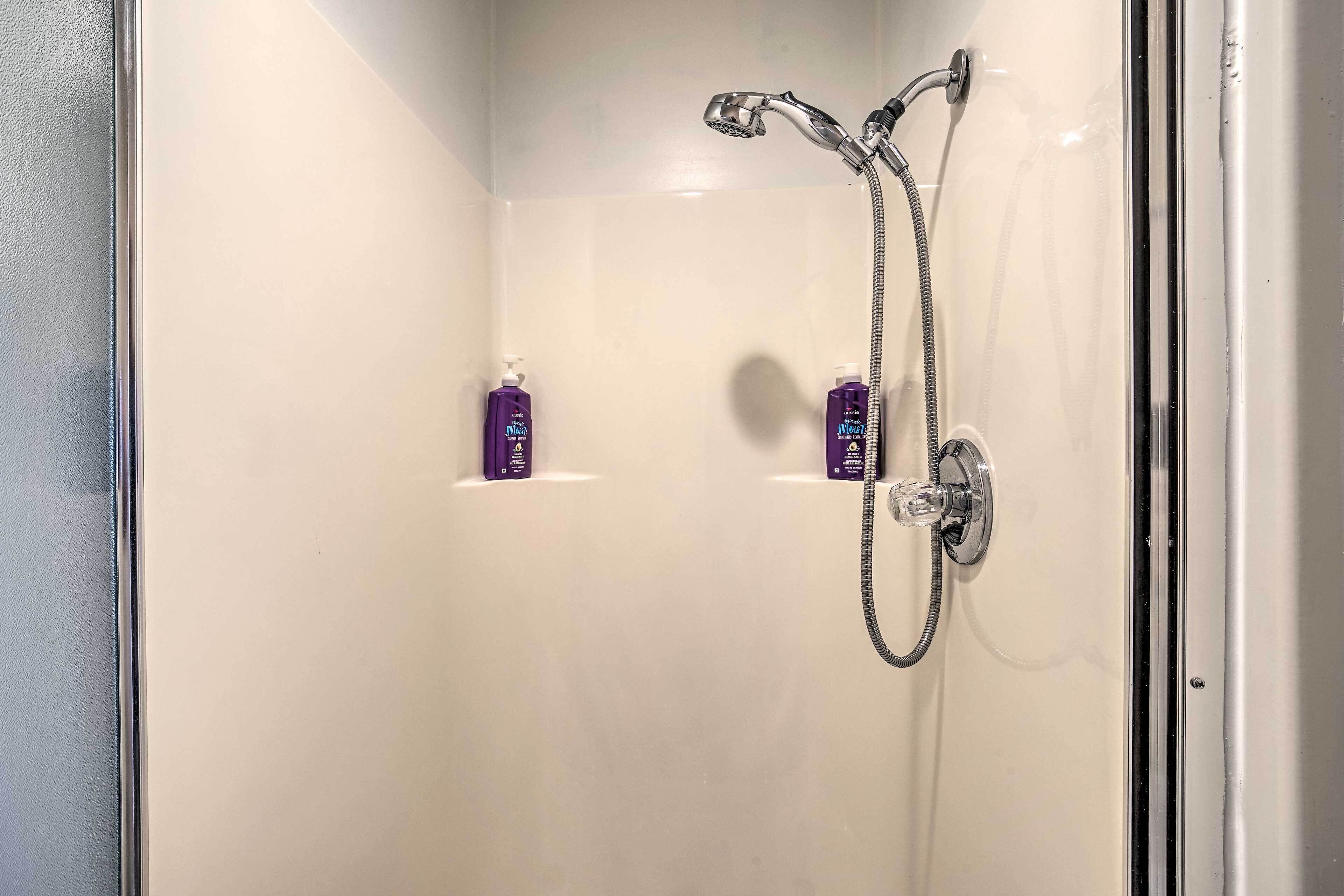Un espace douche équipé d’un pommeau de douche à main et d’un robinet mural. Deux flacons de produits capillaires sont fixés au mur.