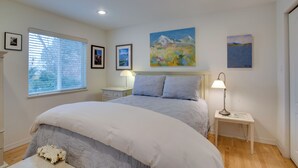 A bedroom with a large bed, a nightstand, a bedside table, and a window with blinds. - Grand Junction Abode ~ 2 Miles to Wineries & Golf! (Grand Junction)