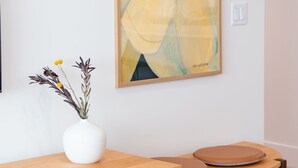 Una sala de estar moderna con una mesa de centro de madera, un jarrón blanco con flores y un cuadro abstracto grande en la pared.