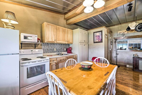 A kitchen with wooden cabinets, a white stove, a microwave, and a dining table with chairs. - Renovated Bunkhouse on 12-acre Horse Farm! (Perrysville)
