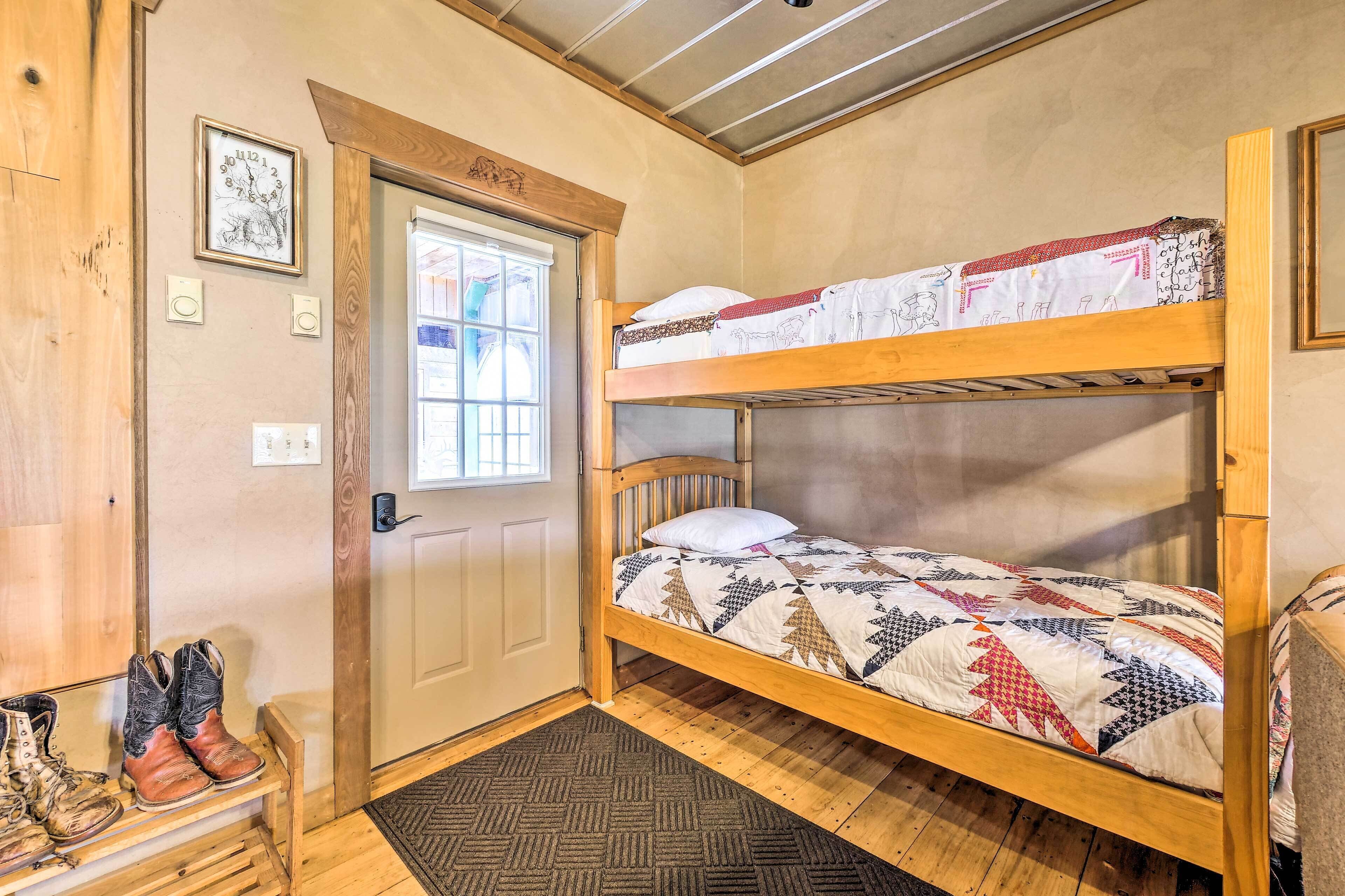 A bunk bed with a patterned quilt, a wooden door with a window, and a pair of boots on a shelf.