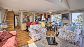 A spacious living area with a wooden staircase, a kitchen, and a dining area with a view of the outdoors.