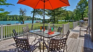 A deck with a table and chairs, surrounded by a white railing, overlooking a lake with boats and greenery. - Waterfront Vandalia House w/ Dock on Donnell Lake! (Vandalia)