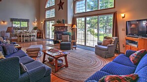 A spacious living room with a fireplace, large windows, and a television. - Waterfront Vandalia House w/ Dock on Donnell Lake! (Vandalia)