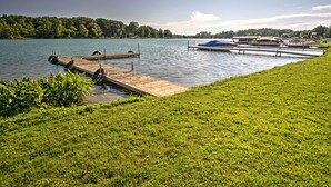 A lakeside dock with boats, a grassy area, and a forested hill in the background. - Waterfront Vandalia House w/ Dock on Donnell Lake! (Vandalia)