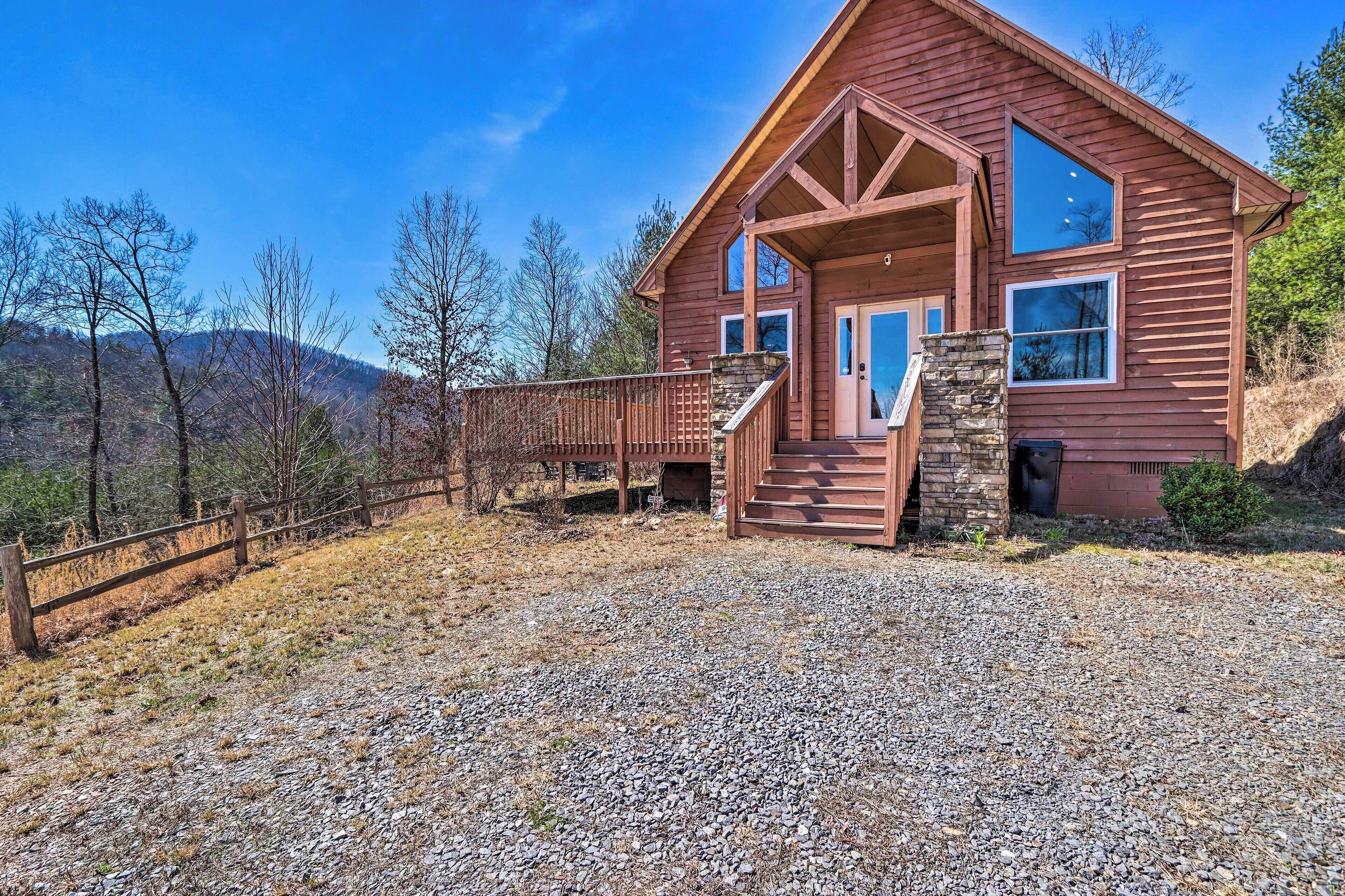 A wooden cabin with a stone staircase, large windows, and a gravel driveway.