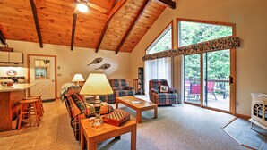 Ein gemütliches Wohnzimmer mit hohen Decken, Holzbalken, einem Kamin und großen Fenstern mit Blick ins Freie.
