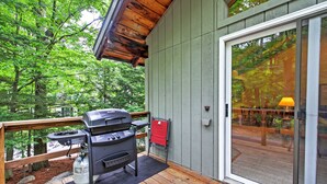 Eine Holzterrasse mit einem Grill, einem roten Klappstuhl und einer Glastür, die zu einem Außenbereich führt.