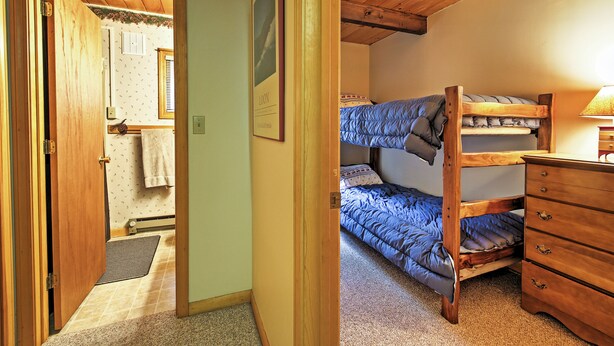Ein Schlafzimmer mit Etagenbett, einem Holzkleiderschrank und einer Tür zu einem anderen Raum.